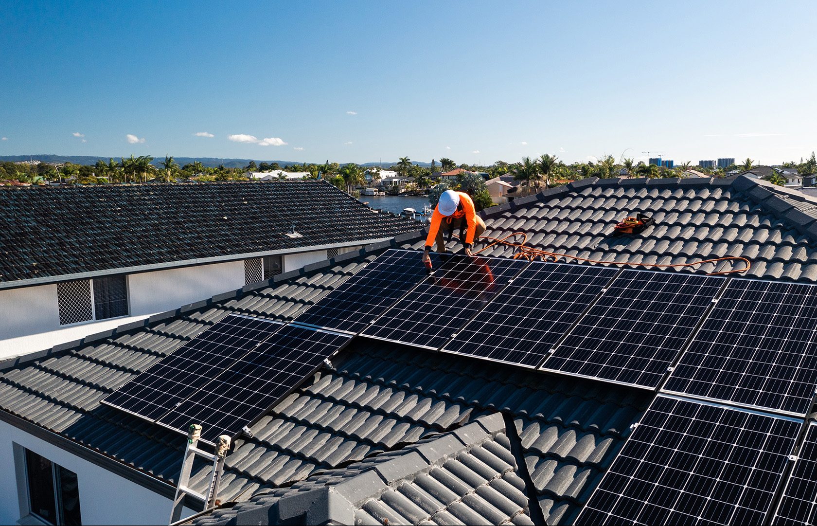 A contractor wearing a hard had and orange shirt installs black solar panels on a black roof.